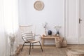 Flowers on wooden stool next to armchair in white loft interior with pouf and plate. Real photo Royalty Free Stock Photo