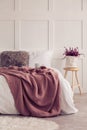 Flowers on wooden stool next to bed with red blanket in white simple bedroom interior Royalty Free Stock Photo