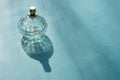 Flowery perfume in beautiful glassy faceted bottle on bright sunlights with long shadow on blue background. Sunlit