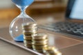 Flowing sand in hourglass with defocused stack of coins on laptop symbolizing market resistance and financial crisis. Royalty Free Stock Photo