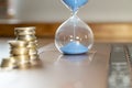 Flowing sand in hourglass symbolizing market resistance and financial crisis. Defocused stacks of coins and laptop Royalty Free Stock Photo
