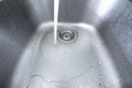 Flowing stream of tap water into a metal kitchen sink. Long exposure, no people, wide angle Royalty Free Stock Photo