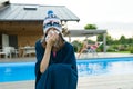 Flu, colds in the summer. Girl in a knitted hat with plaid with handkerchief sneezes, wipes her nose. Background nature, pool, gir Royalty Free Stock Photo