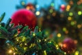 Fluffy branches of a Christmas tree with garlands against a background of red Christmas balls in out of focus Royalty Free Stock Photo