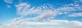 Fluffy cirrus clouds float slowly high in the azure blue sky on a sunny day. Panoramic skyscape of many small white clouds are