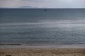 Fluffy grey-blue clouds meet calm dark blue sea far from the sandy coast. Mountains background, space