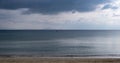 Fluffy grey-blue clouds meet calm dark blue sea far from the sandy coast. Mountains background, space