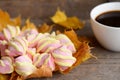 Fluffy marshmallow candy on yellow leaves, a cup of coffee on a wooden table. Light fall breakfast or snack concept. Rustic style