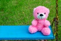 Fluffy pink teddy bear sitting on blue vintage swing