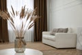 Fluffy reed plumes on white table in living room interior. Space for text