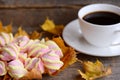 Fluffy sweet marshmallow candy on a plate, a cup of coffee, yellow leaves on a wooden table. Fall breakfast or snack concept