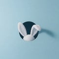 Fluffy white rabbit ears peek through a round hole in a light blue background, casting a subtle shadow. Generative AI Royalty Free Stock Photo