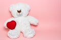 Fluffy white teddy bear holding a red heart on a pink background