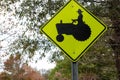 Fluorescent green triangular yield sign with the silhouette of a farmer on a tractor with trees in the background Royalty Free Stock Photo