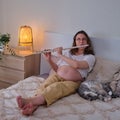 Flute in the hands of a pregnant woman on a home bed, rest and learning musical instruments of the expectant mother