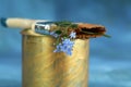 A fluted brush in golden paint with a branch of forget-me-nots in the bristles on a blue background. Selective focus