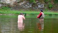 Fly fishing. A photographer with a naked torso waist-deep in water photographs a fisherman. in red clothes. Sports and