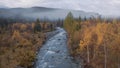 Flying along cold river and colorful autumn forest covered by fog and low clouds. Clip. Natural landscape with a wild Royalty Free Stock Photo