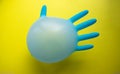 Flying blue rubber surgical glove in the form of a balloon on a yellow background with a copy of space. The concept of minimalism