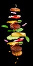 Flying burger ingredients: cutlet, sesame seed bun, tomato, onion, green lettuce, cheese on black background Royalty Free Stock Photo