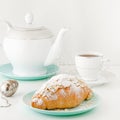 Flying food concept. Powdered sugar falling on freshly baked croissant on white breakfast table with teapot and tea.