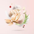 Flying Garlic falling in air with red and black pepper and herbs like dill and fennel leaves on light pink background. Spicy and