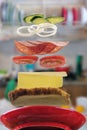 Flying layers of sandwich with ham, cheese, vegetables over the red plate with blurred kitchen background. Breakfast food concept Royalty Free Stock Photo