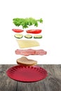 Flying layers of sandwich; ham; cheese; vegetables and red plate over the wooden table Royalty Free Stock Photo