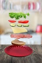 Flying layers of sandwich, ham, cheese, vegetables and red plate over the wooden table. Breakfast food concept Royalty Free Stock Photo