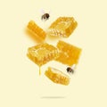 Flying pieces of honeycomb, drop of honey and bees on a yellow background. A conceptual composition of floating honeycombs.