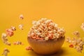 Flying popcorn from wooden bowl on yellow background.