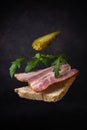 a flying sandwich made from a slice of bread, pork belly, arugula leaves and canned cucumber on a dark gray background with a
