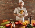 Young Caucasian red-bearded man, chef cooking fresh vegetable salad in cafe, restaurant kitchen. Concept of a correct Royalty Free Stock Photo