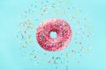 Flying sprinkled pink donut. Sweet doughnut on pastel blue background