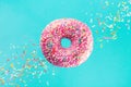 Flying sprinkled pink donut. Sweet doughnut on pastel turquoise background