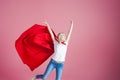 Flying superhero. Funny young woman in the image of a superhero to the rescue. Pink background