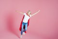 Flying superhero. Funny young woman in the image of a superhero to the rescue. Pink background