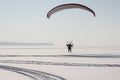 The flying-up person on a motorized paraglider against a snow surface of the river Royalty Free Stock Photo