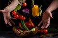 Flying vegetables for salad between male hands. Healthy vegetarian food is levitation over a wooden bowl on a dark stone table