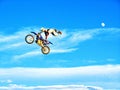 FMX motorbike rider completing stunts against the backdrop of a blue sky with clouds and the moon Royalty Free Stock Photo