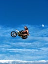 FMX motorbike rider completing stunts against the backdrop of a blue sky with clouds and the moon Royalty Free Stock Photo