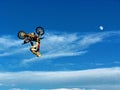 FMX motorbike rider completing stunts against the backdrop of a blue sky with clouds and the moon