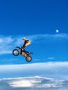 FMX motorbike rider completing stunts against the backdrop of a blue sky with clouds and the moon