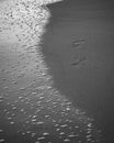 Foam bubbles of the sea waves and the footprints on the beach black and white photograph Royalty Free Stock Photo