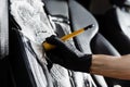 Foam cleaning black leather seat using brush. Worker in auto cleaning service clean car inside. Car interior detailing. Royalty Free Stock Photo