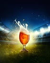 Foam and drops. Glass of cool lager beer standing on grass at football stadium over evening sky with flashlights. Game Royalty Free Stock Photo