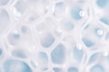 Foam texture on blue background, macro. Soap, shampoo, shower gel foam, face cleansing mousse or bubble mask sample. White