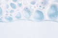 Foam texture on blue background, macro. Soap, shampoo, shower gel foam, face cleansing mousse or bubble mask sample. White