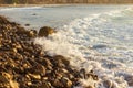 Foaming pastel wave washing across bay with distant wave backwash, breaking on rocky shoreline Royalty Free Stock Photo