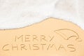 Foaming sea wave coming to wash Merry Christmas inscription on w Royalty Free Stock Photo